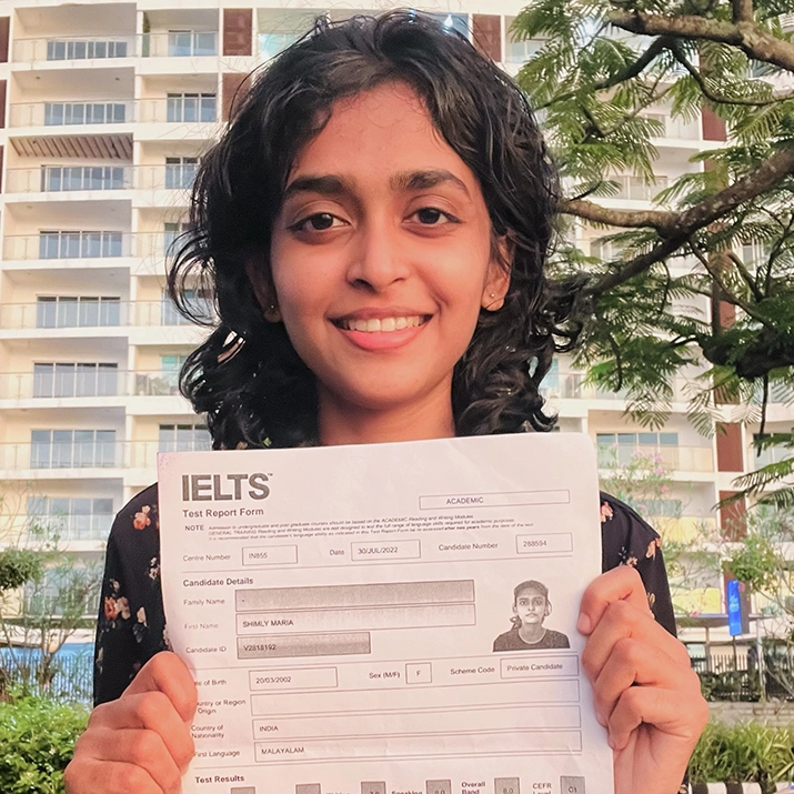 Student holding an IELTS test report form and smiling outdoors