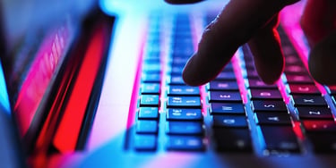 Hand reaching towards a laptop keyboard illuminated with blue and red light