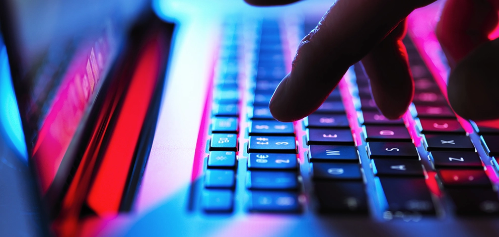 Hand reaching towards a laptop keyboard illuminated with blue and red light