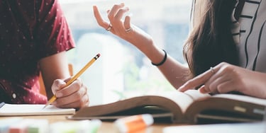 Students discussing study notes while writing in a notebook during IELTS preparation