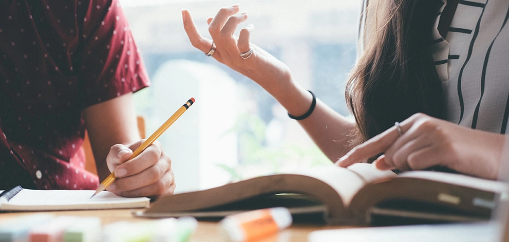 Students discussing study notes while writing in a notebook during IELTS preparation
