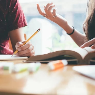 Students discussing study notes while writing in a notebook during IELTS preparation