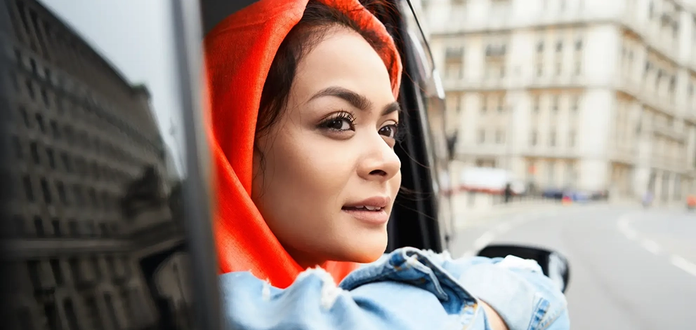 Student wearing a red hoodie looking out of a car window in a city - right