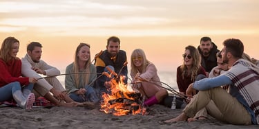 Group of friends sitting around a campfire on a beach in the evening