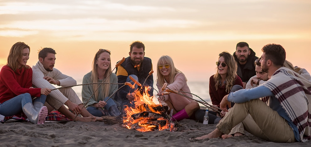 Group of friends sitting around a campfire on a beach in the evening