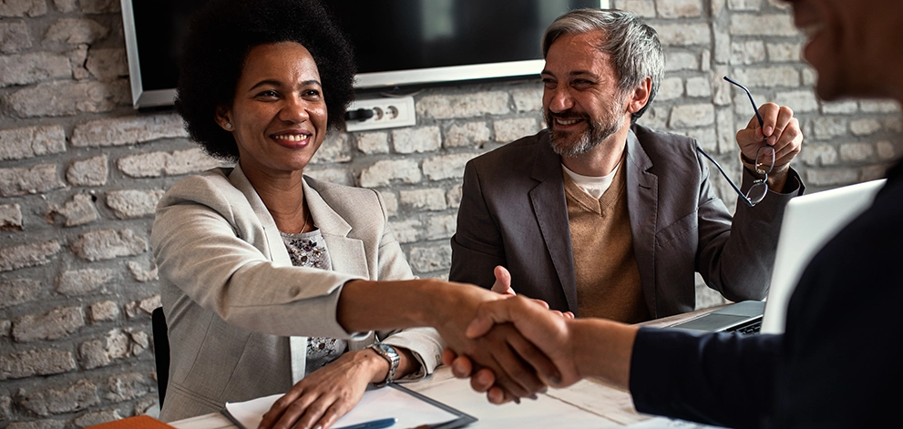 Two people shaking hands during a business meeting across a table