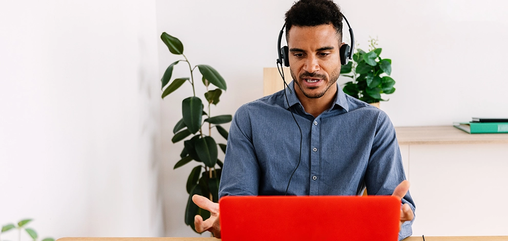 IELTS speaking practice online with a man wearing a headset talking to a laptop at a desk