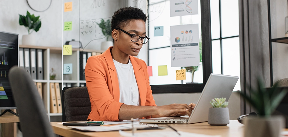 Professional working on a laptop at a desk with charts and notes on a board