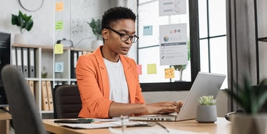 Professional working on a laptop at a desk with charts and notes on a board