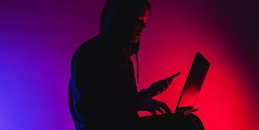 Person using a laptop and smartphone in dark surroundings