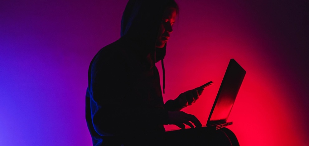 Person using a laptop and smartphone in dark surroundings