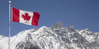 Canadian flag flying in front of snow-covered mountains under a clear sky