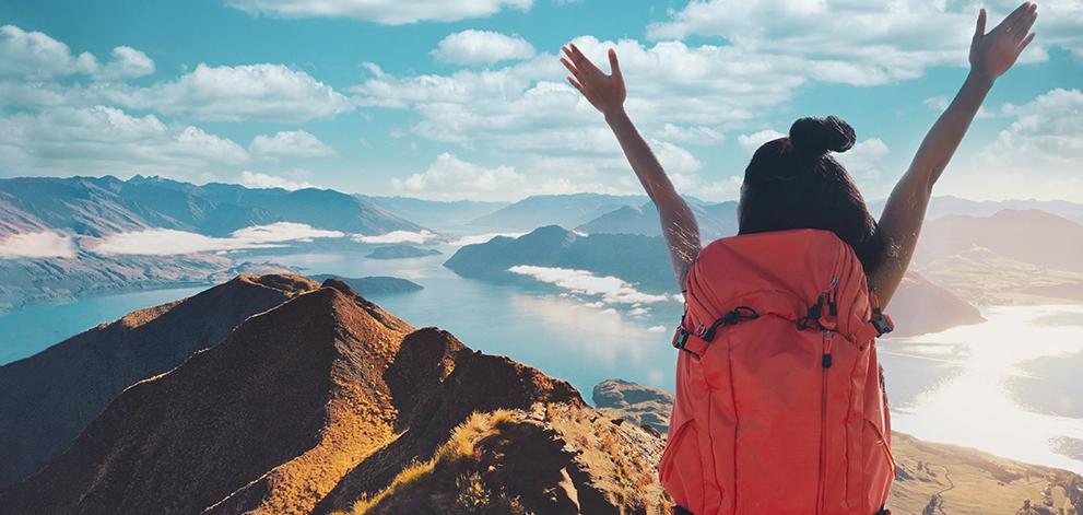 Person with a backpack standing on a mountain overlooking a lake and landscape