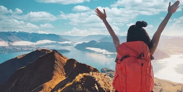 Person with a backpack standing on a mountain overlooking a lake and landscape