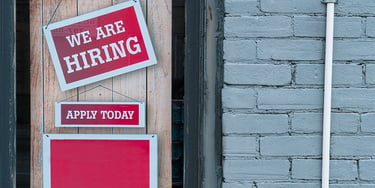 We are hiring sign displayed in a shop window with apply today message