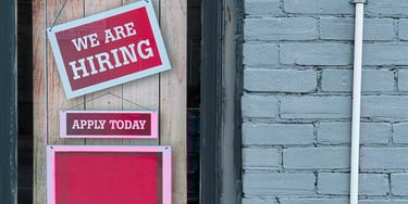 We are hiring sign displayed in a shop window with apply today message