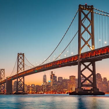 San Francisco Bay Bridge lit at sunset with city skyline in the background