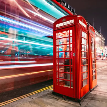 Red telephone box on a London street at night with blurred traffic lights