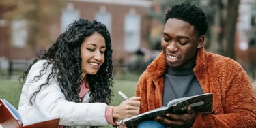Male and female students holding notebooks while sitting on grass