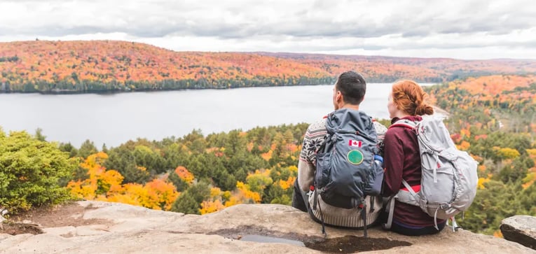 Couple sitting on a rock ledge overlooking a panoramic autumn landscape with lake and hills