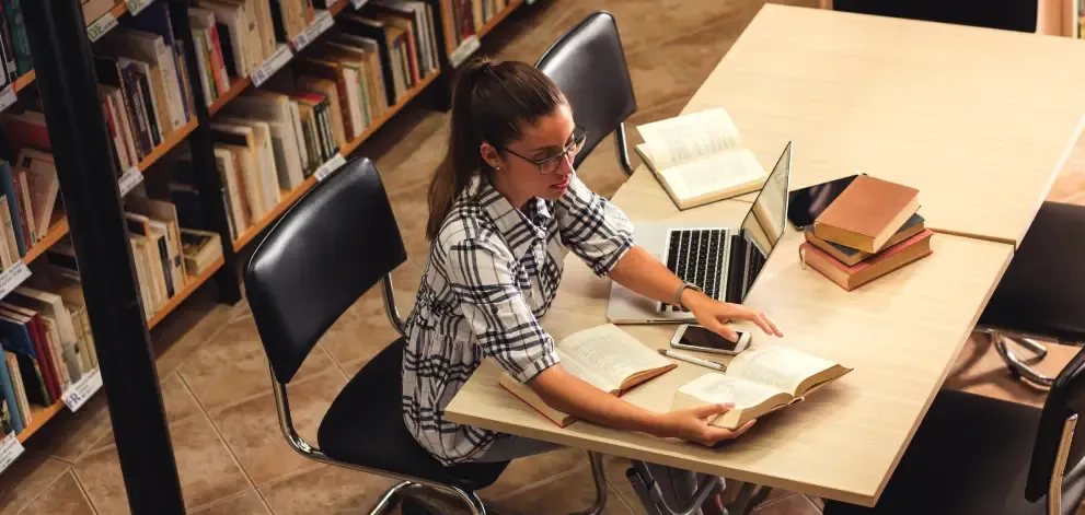 Young female student studying in a library with laptop and books