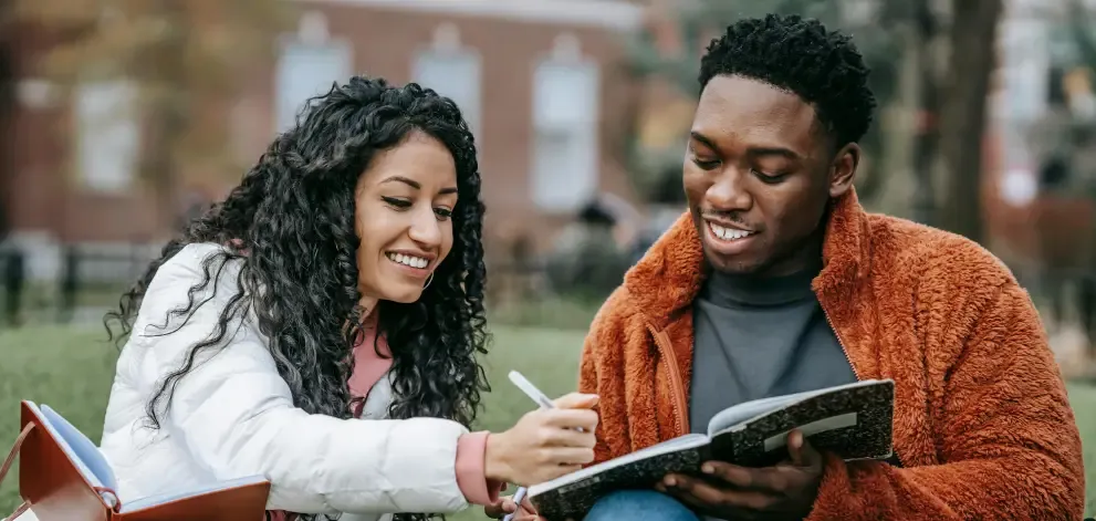 Male and female students sitting on grass holding notebooks and studying together