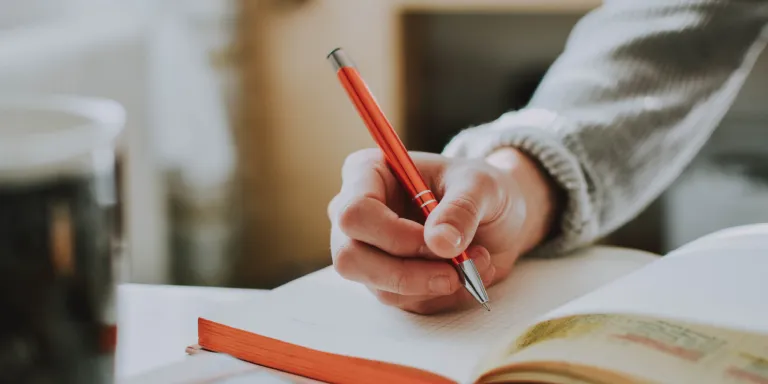 Person writing in a book with an orange pen