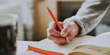 Person writing in a book with an orange pen
